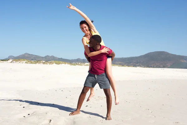 Young man carrying girlfriend on his back on beach — Stock Photo, Image