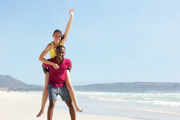 Giovane uomo piggybacking fidanzata in spiaggia — Foto Stock