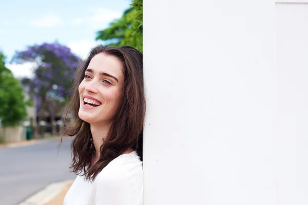 Smiling woman leaning against white wall — Stock Photo, Image