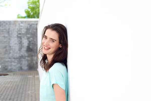 Confident lady smiling leaning against white wall — Stock Photo, Image