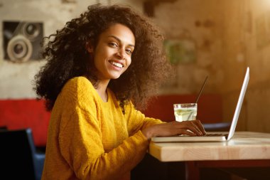 Dizüstü bilgisayar ile bir kafede oturan gülümseyen kadın