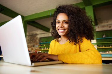 Dizüstü bilgisayar ile bir kafede oturan neşeli Bayan