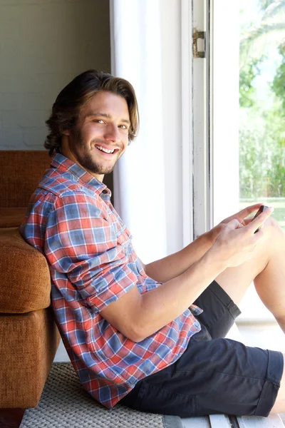 Sonriente joven sentado en el suelo con teléfono celular — Foto de Stock