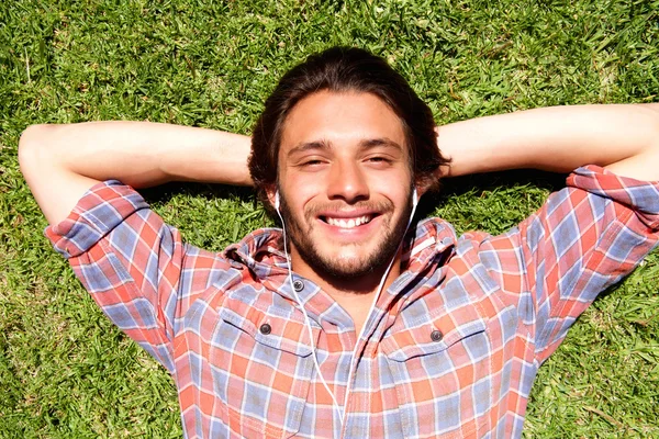 Lachende jonge man liggen in het gras — Stockfoto