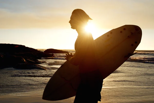 Young man carrying a surfboard at sunset — Stock Photo, Image