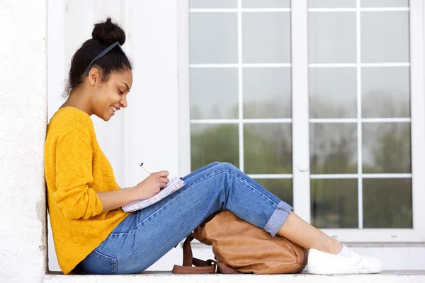 Joyeux jeune femme assise dehors à écrire un livre — Photo