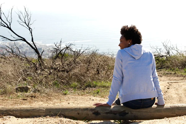 Young woman sitting outdoors on a log — Stock Photo, Image