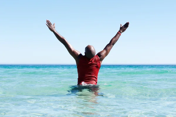 African man standing in sea with his hands raised — Stock Photo, Image