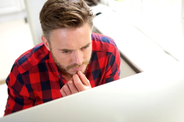 Homem de negócios atraente pensando atrás da tela do computador — Fotografia de Stock