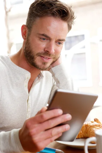 朝食を食べながらタブレットで見ているハンサムな男 — ストック写真