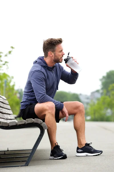 Sportler sitzt auf Bank und trinkt Wasser — Stockfoto