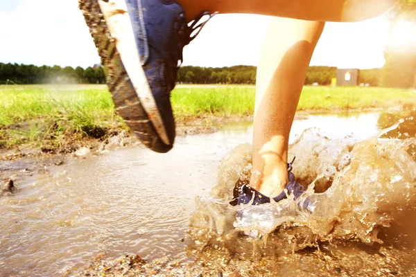 Runner's sneakers splashing in mud puddle — Stock Photo, Image