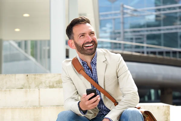 Ridere uomo maturo seduto all'aperto con il cellulare — Foto Stock