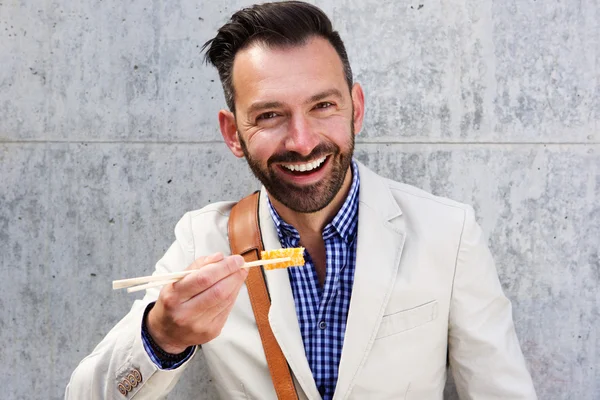 Un homme souriant mange des sushis avec des baguettes — Photo