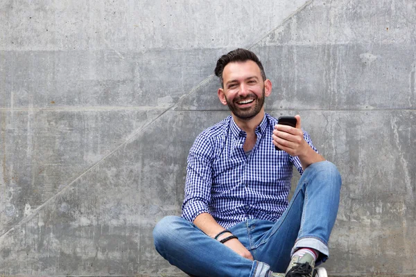 Felice ragazzo maturo seduto contro un muro e sorridente — Foto Stock