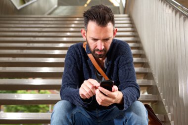 Cep telefonu kullaranarak merdivenlerde oturan olgun adam