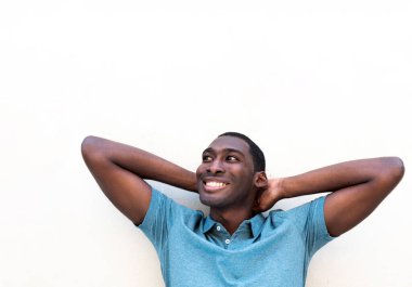 Kapalı portre, rahat genç siyah adam gülümsüyor. Elleri başının arkasında beyaz arka planda.