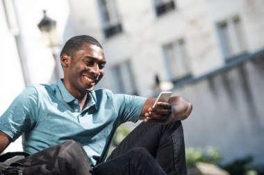 Kapalı portre, gülümseyen Afrikalı Amerikalı genç adam dışarıda cep telefonuna bakıyor.