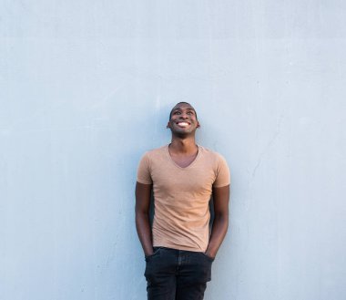 Havalı genç Afrikalı Amerikalı adam gri duvara yaslanmış ve yukarı bakıyor.