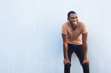 Portre mutlu genç siyah adam elleri dizlerinin üzerinde gri arka planda