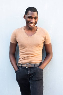 Yakışıklı genç zenci adam gülümsüyor ve gri duvara yaslanıyor.