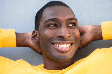 Kapalı portre, gülümseyen, elleri başının arkasında olan Afrikalı Amerikalı genç bir adam.