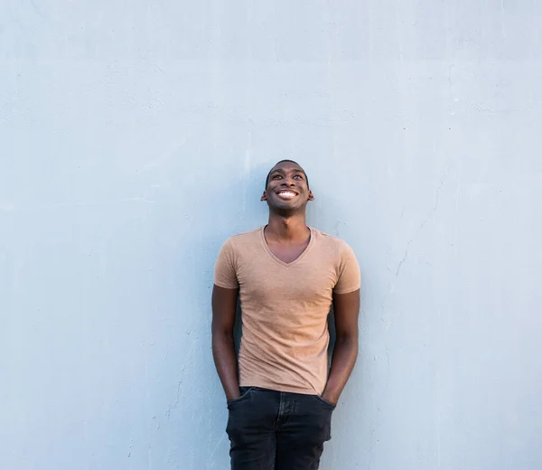 Portrait cool young African American guy leaning against gray wall and looking up