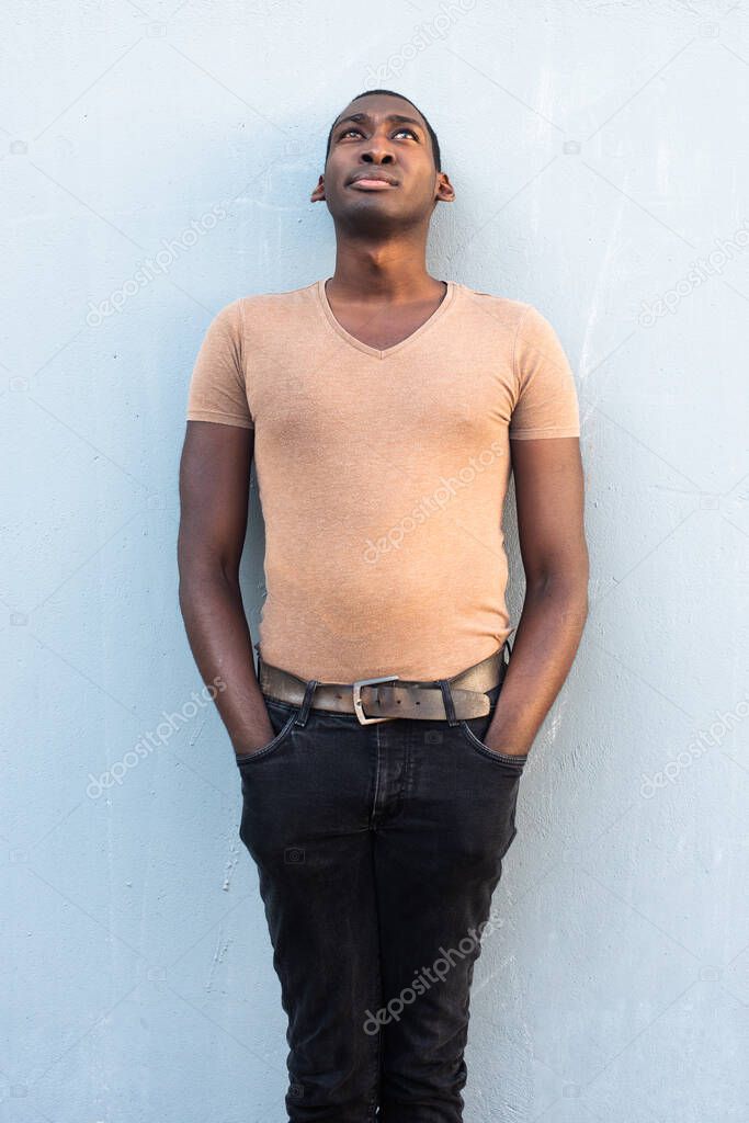 Portrait handsome young African American man leaning against gray wall and looking up with serious expression