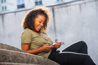 Yandan çekilmiş genç bir kadın. Dışarıda dinleniyor. Cep telefonuna bakıyor.