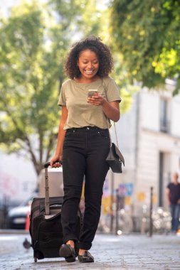 Şehirde çanta ve cep telefonuyla gezen mutlu genç bir kadın portresi.