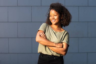 Kolları gri arka planda olan mutlu, Afro-Amerikan bir kadın portresi.