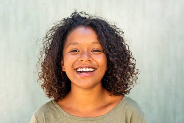 Yeşil arka planda gülümseyen kıvırcık saçlı Afro-Amerikalı genç bir kadın.