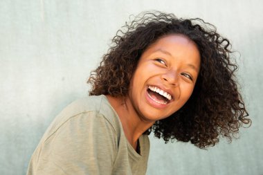 Yakın plan mutlu, kıvırcık saçlı, yeşil arka planda kahkahalar atan genç kadın. 