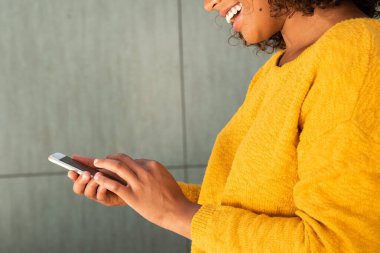 Yan bakış açısını kapat. Elinde cep telefonu tutarken gülümseyen genç kadın.