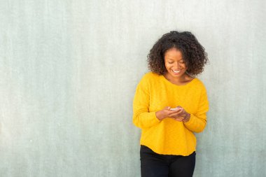 Gülümseyen genç bir kadın yeşil arka planda cep telefonuna bakıyor.