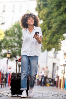 Cep telefonuyla yürüyen ve bavulu çeken Afro-Amerikalı genç bir portre.