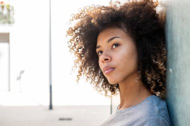 Yan portreyi kapatın. Ciddi bir Afrikalı Amerikalı kız dışarıda duvara yaslanıyor.