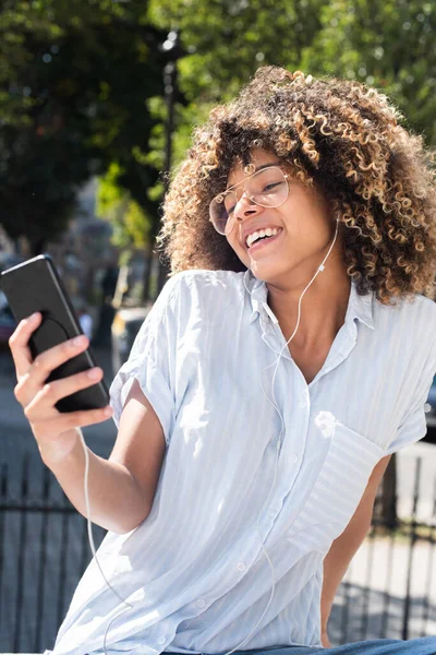 Retrato Feliz Joven Afroamericana Mujer Mirando Teléfono Móvil Mientras Escucha — Foto de Stock