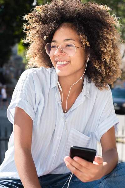 Ritratto Sorridente Giovane Donna Afroamericana Seduta Fuori Con Cellulare Auricolari — Foto Stock