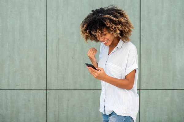 ポートレート幸せな若いアフリカ系アメリカ人女性見ます携帯電話によって緑の壁 — ストック写真