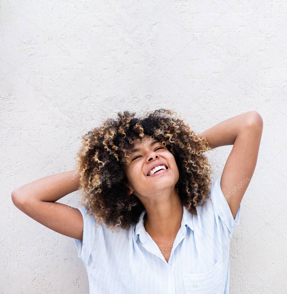 Portrait laughing african american young woman with hands in curly hair by white background 
