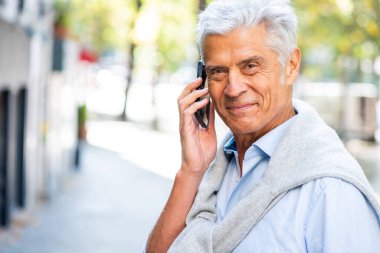 Yakışıklı yaşlı bir adamın cep telefonuyla konuştuğu yatay portreyi kapat.