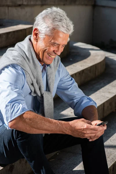 Portret Uśmiechniętego Starszego Mężczyzny Siedzącego Schodach Przy Użyciu Telefonu Komórkowego — Zdjęcie stockowe