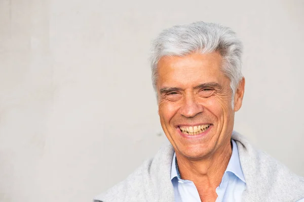 Close up horizontal portrait of older man smiling against white wall