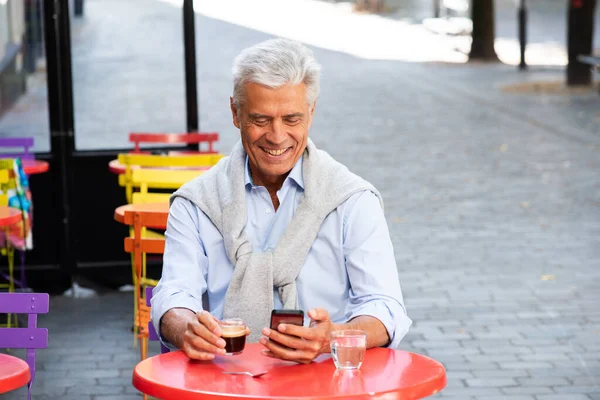 Portrait of older man smiling with cup of coffee and mobile phone in hand