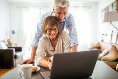 Evde laptopa bakan yaşlı bir çiftin portresi.