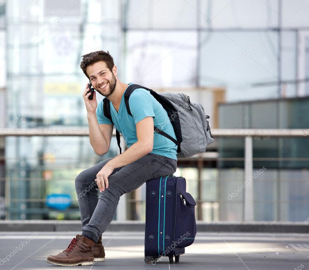Young man sitting on suitcase and calling by cellphone