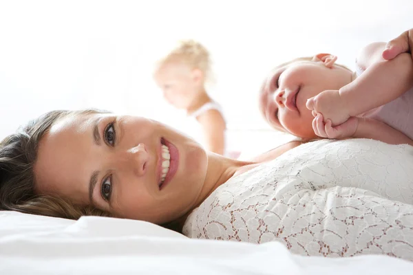 Vacker mor leende i sängen med baby — Stockfoto