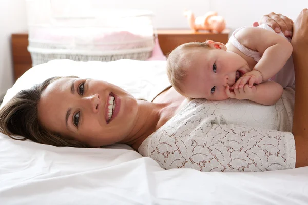 Mulher atraente sorrindo na cama com bebê bonito — Fotografia de Stock