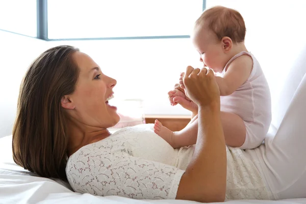Hermosa madre sonriendo con el bebé en la cama —  Fotos de Stock